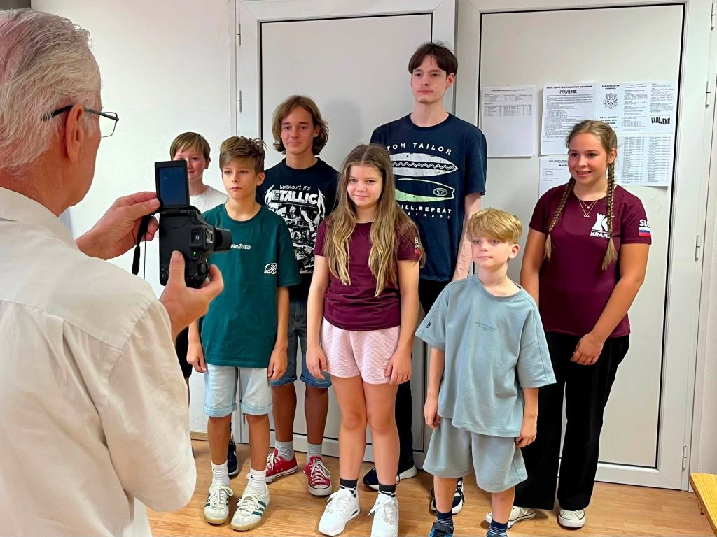 Udeleženci odprtega prvenstva Komende pozirajo za skupinsko fotografijo; na steni sta razpis in lestvica turnirja